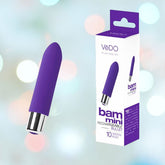The image shows a compact, indigo, bullet-shaped adult novelty product with a silver base placed next to its packaging box. The text on the box reads "VeDO Bam Mini Rechargeable Bullet Vibrator" and highlights "10 VIBRATION MODES." The background features soft, pastel colors that are gently blurred.